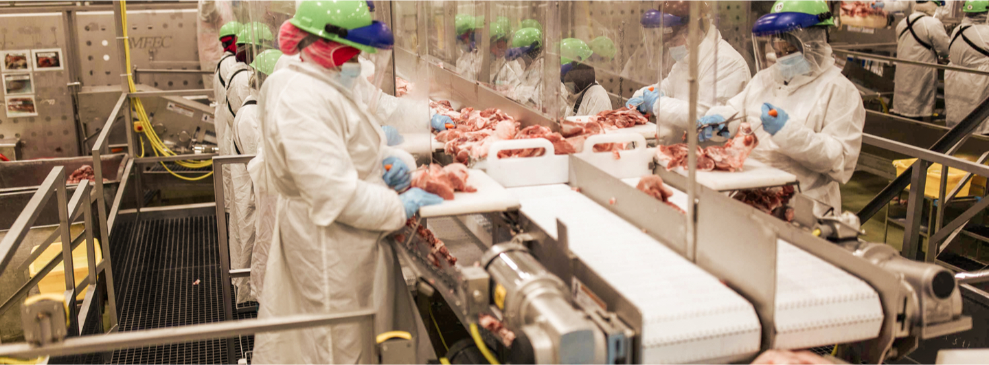 employees in PPE working on a meat assembly line observing safety and quality standards